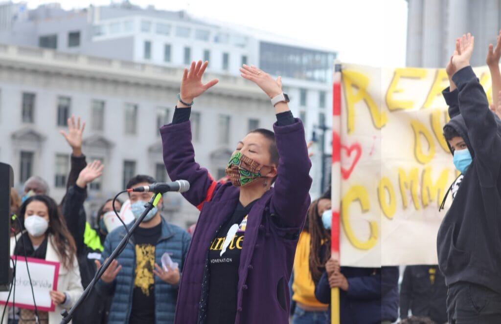 Sassana Yee of Communities of One leads rally participants in prayer at the San Francisco Day of Action in Civic Center Plaza