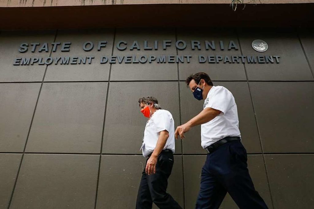Masked individuals walk by the Employment Development Department