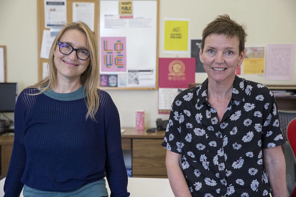 Two white women smile for the camera. They are inside an office.