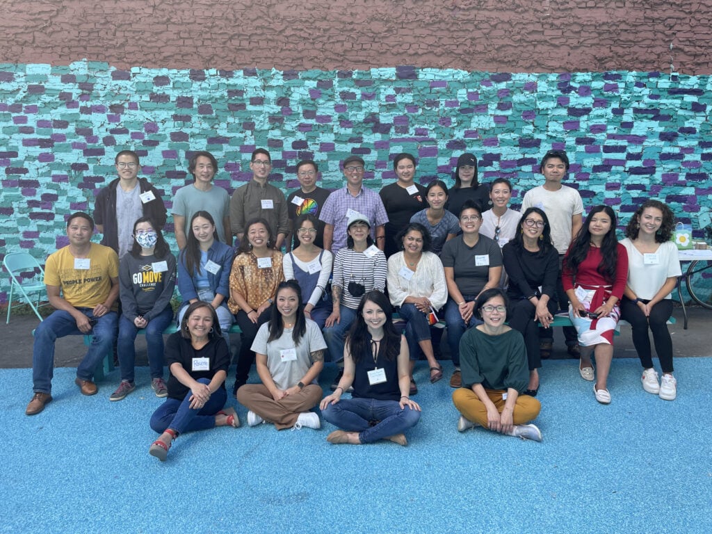 The staff of CAA post for a photo in front of a colorful blue and purple wall. There are 25 people.