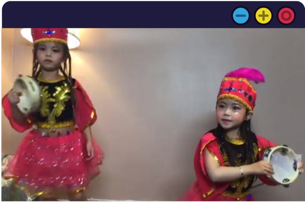 Two East Asian girls, wearing red costumes, perform a dance. They are holding tambourines.