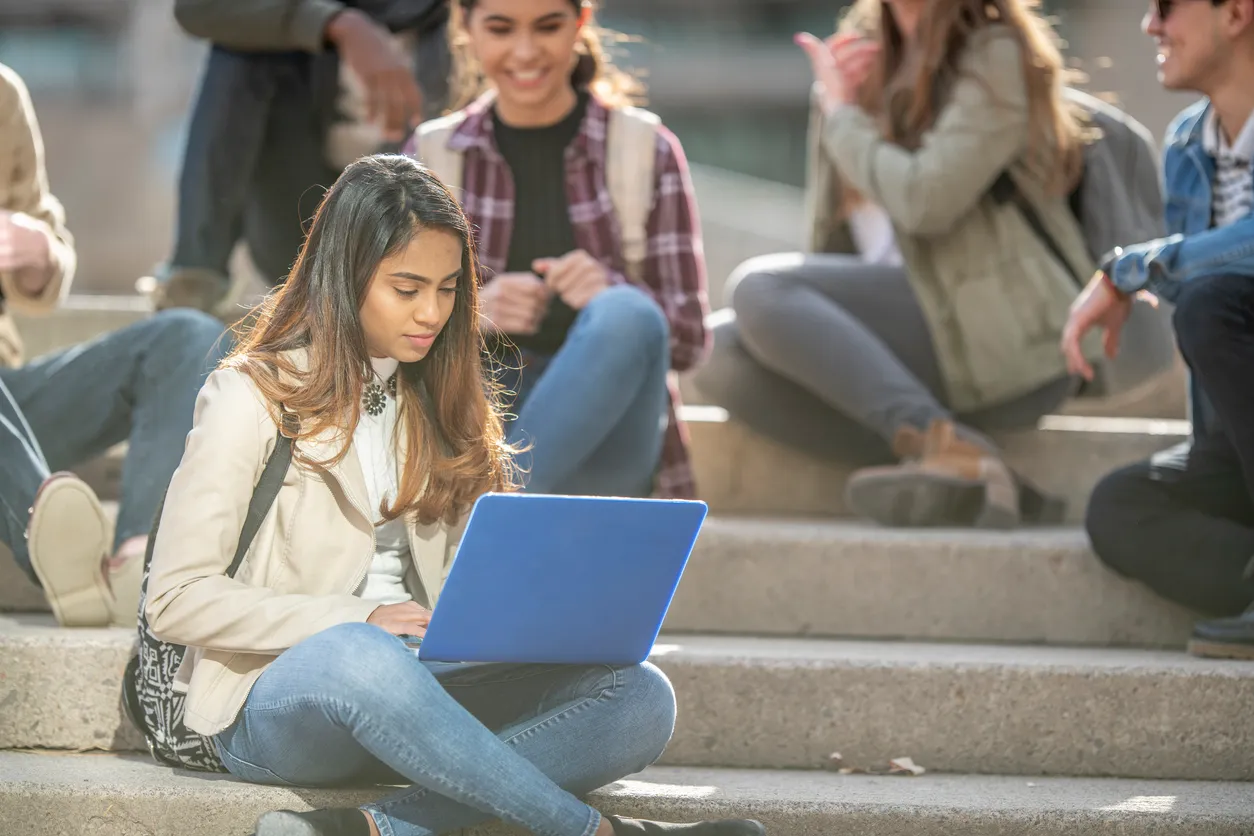 Image of a college age girl sitting with her laptop on campus