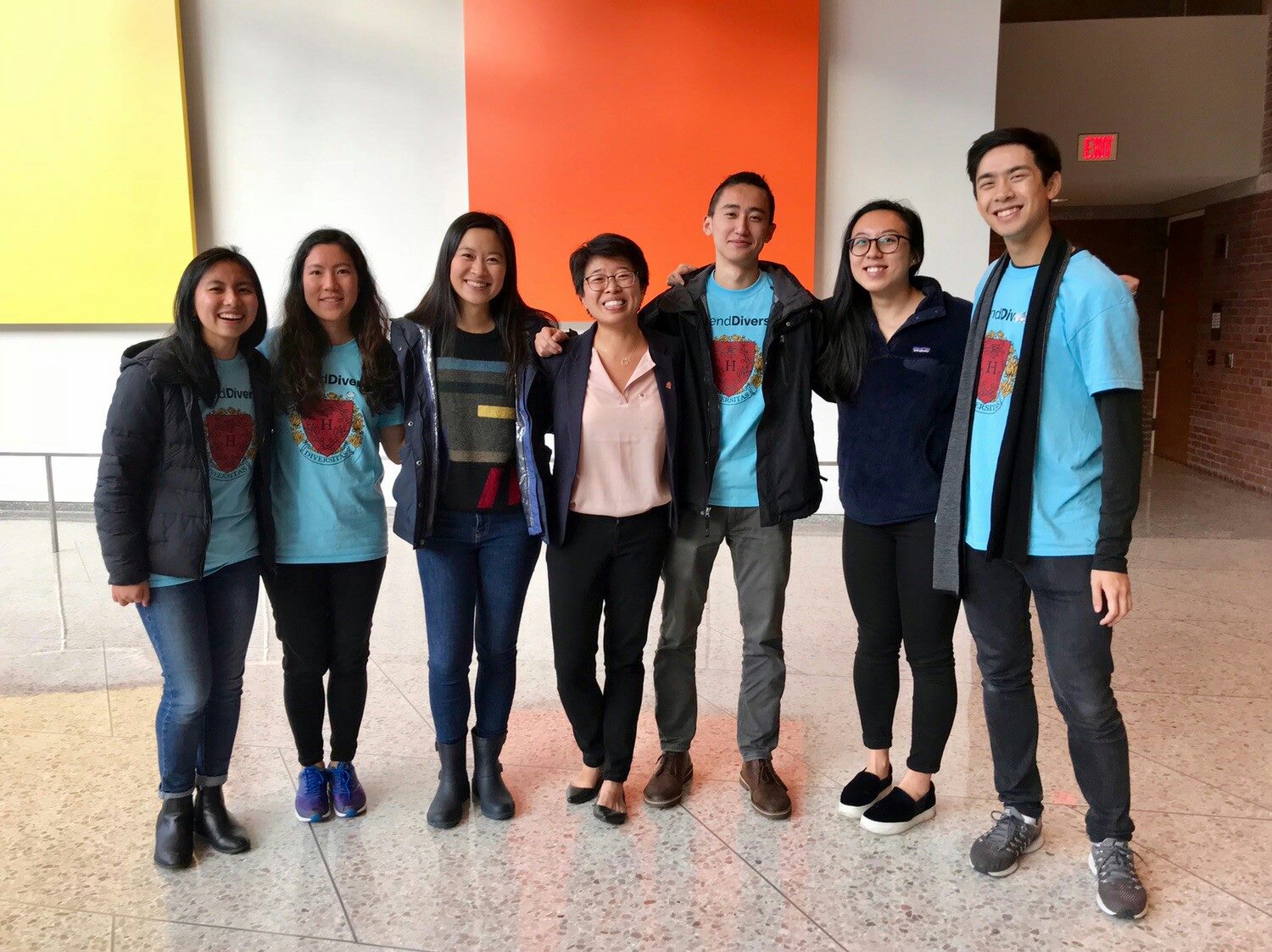 Seven Asian American students pose together for a photo. Many of them are wearing a T-shirt that says, "Defend Diversity"