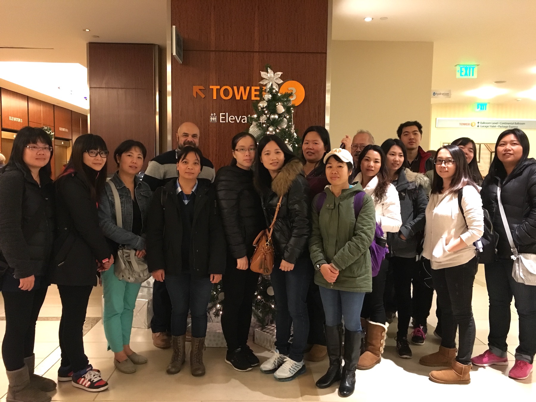 A group of 16 people, mostly Asian, pose together for a photo in the lobby of a hotel